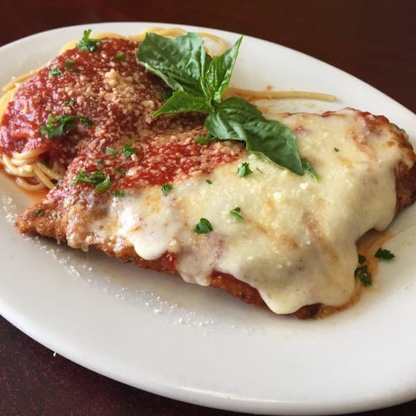Chicken parmesan with spaghetti, red sauce, melted cheese, and basil on a white plate.